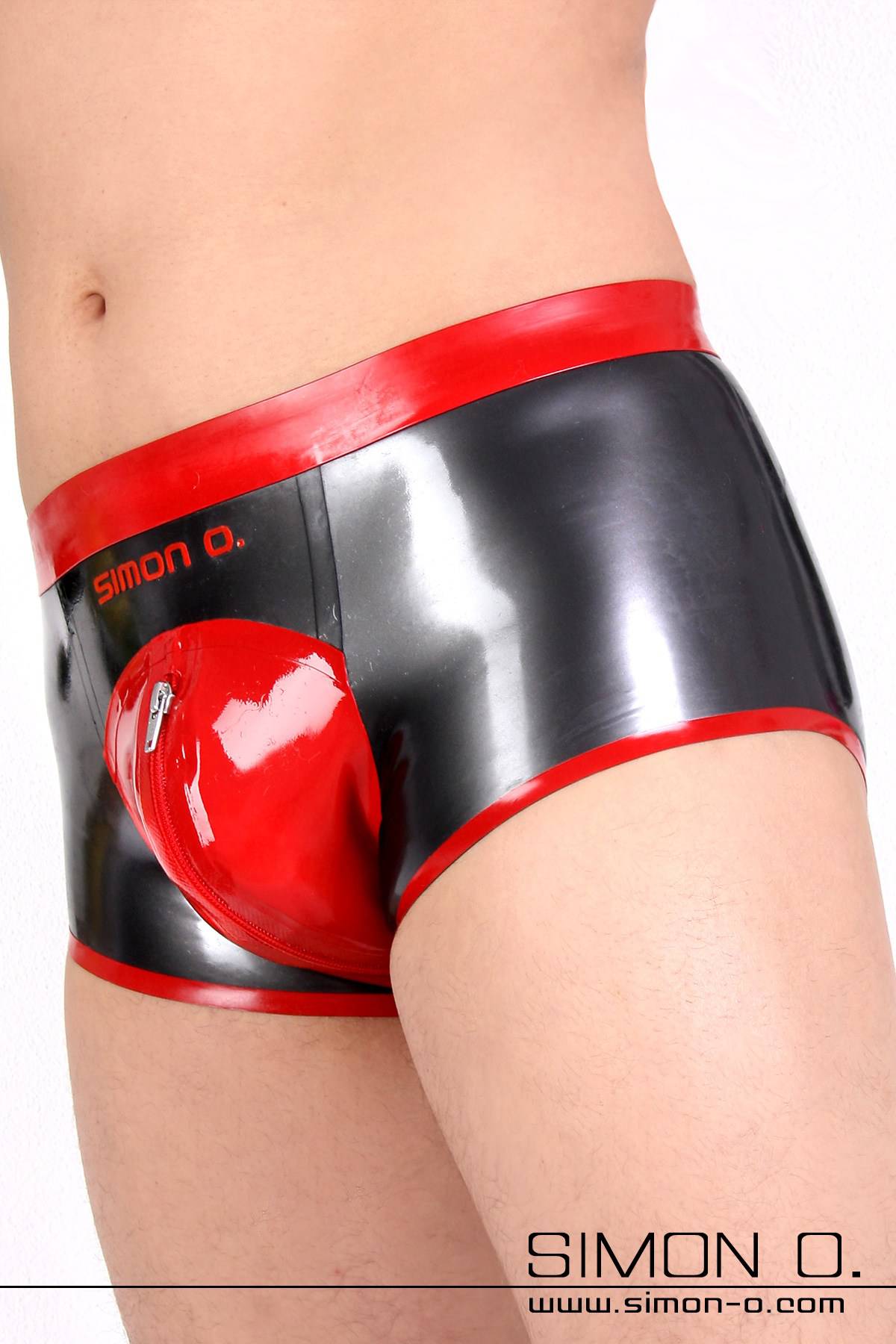 Ein Mann trägt eine glänzende Herren Latex Shorts mit Zipp im Schrittbereich, in der Farbe metallic grau mit Rot kombiniert.