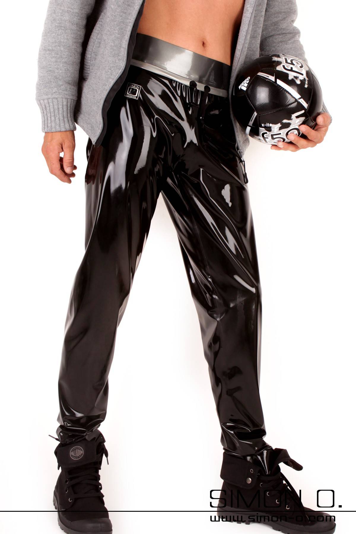 A man is wearing a black shiny training pants made of latex with a jacket and a ball in his hand