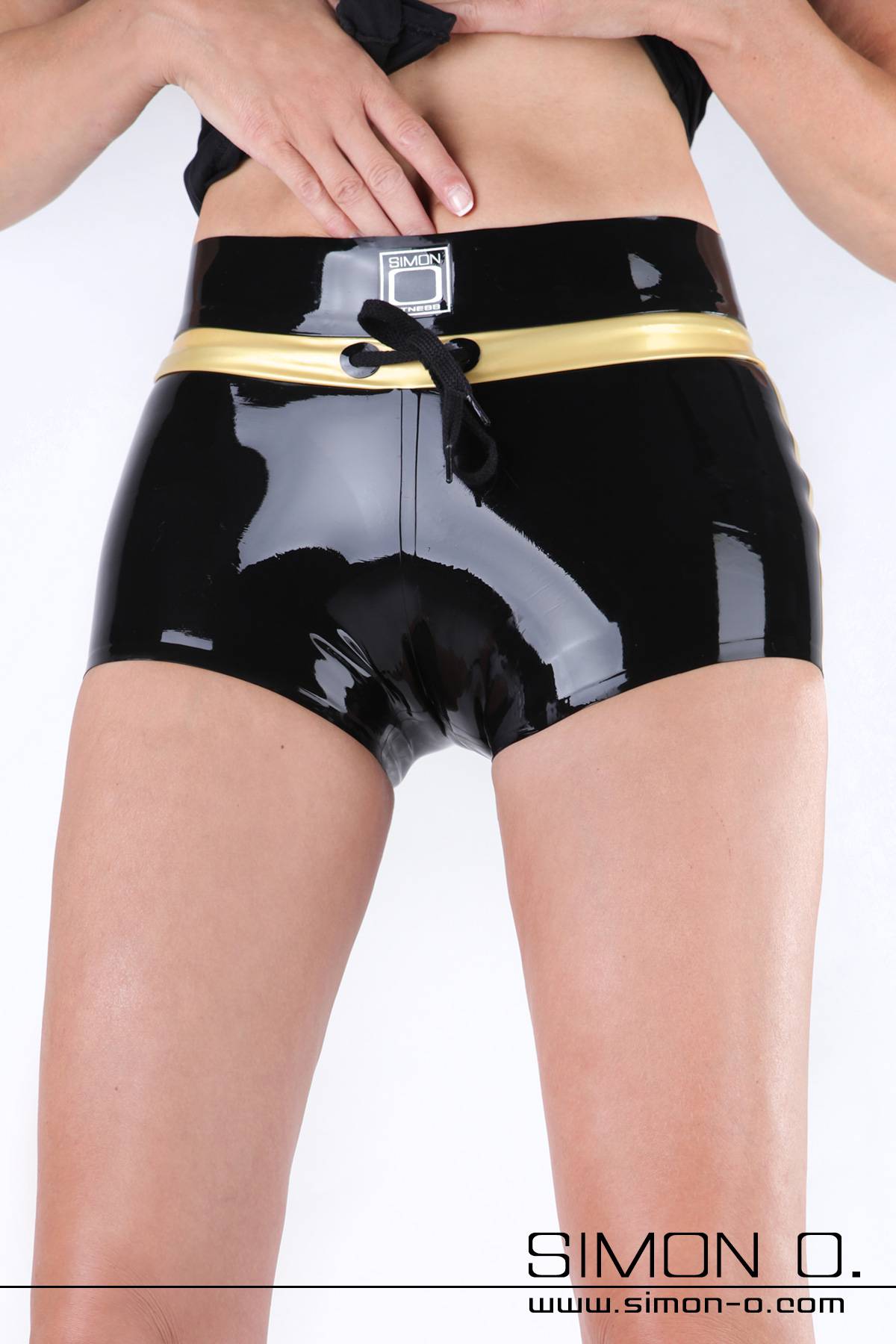 A woman wears a sporty latex hot pants in shiny black with gold applications