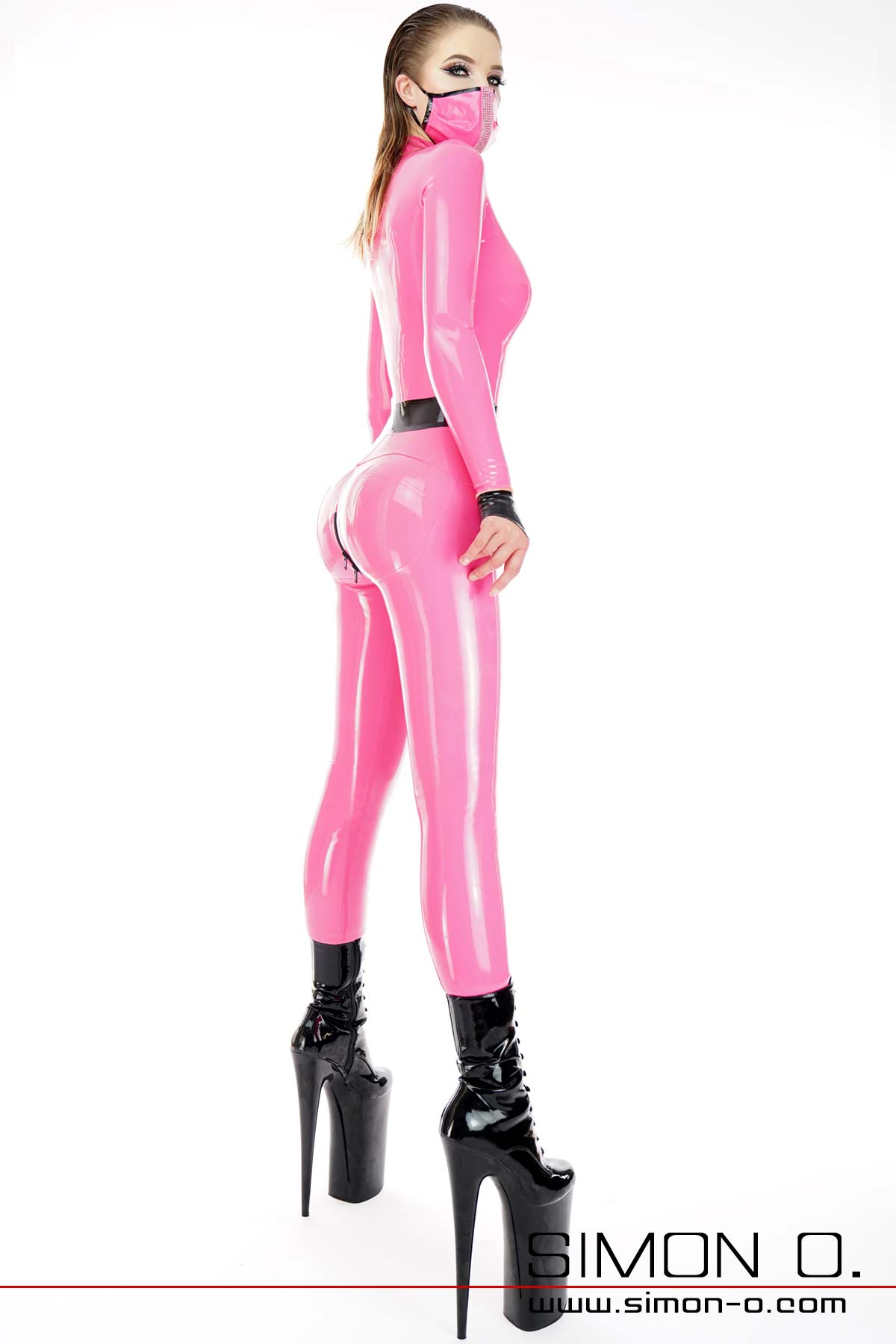 A slim model wears a latex catsuit with push up buttocks area. The latex catsuit has the color pink combined with black. 