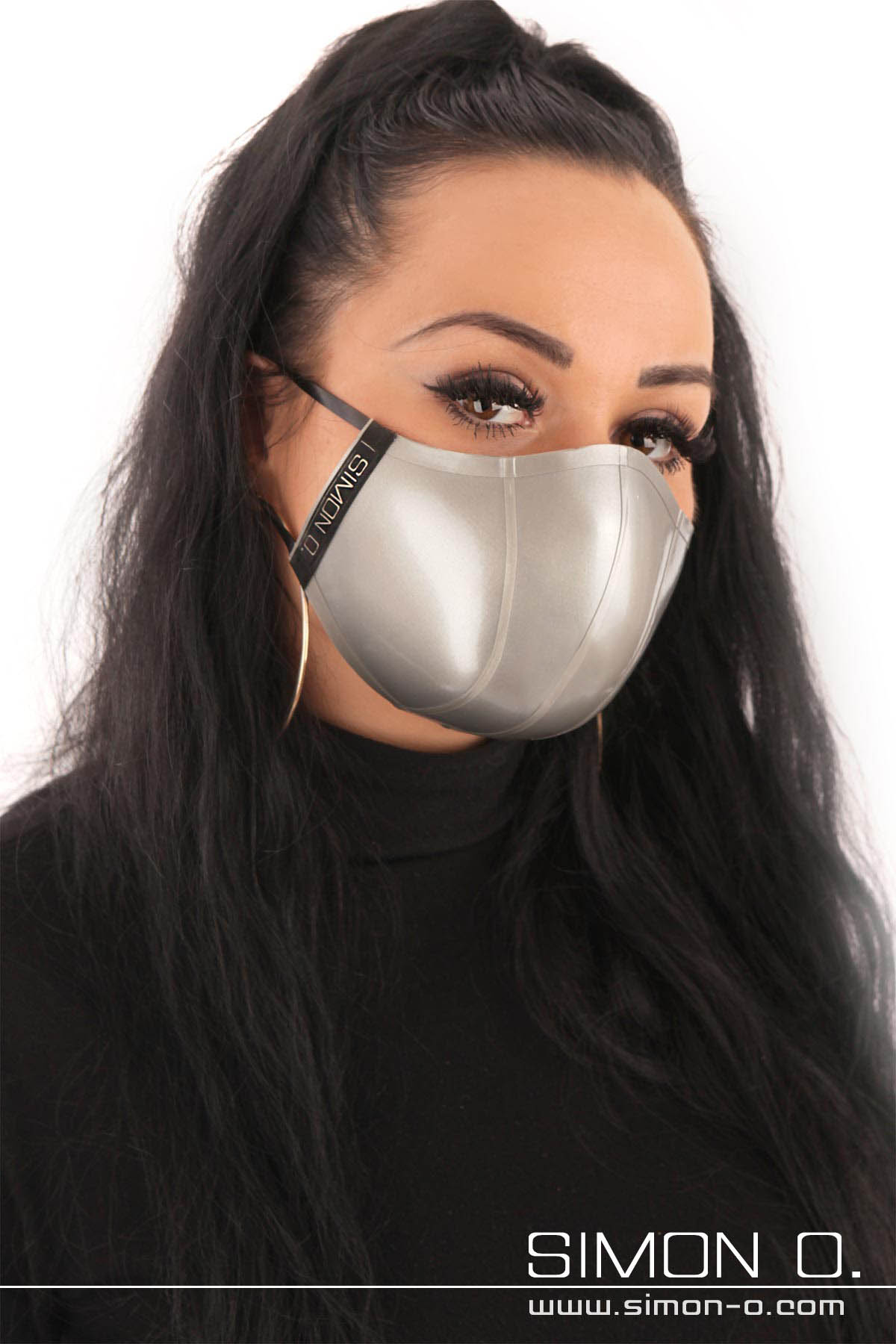 A woman with long black hair wears a silver latex face mask.