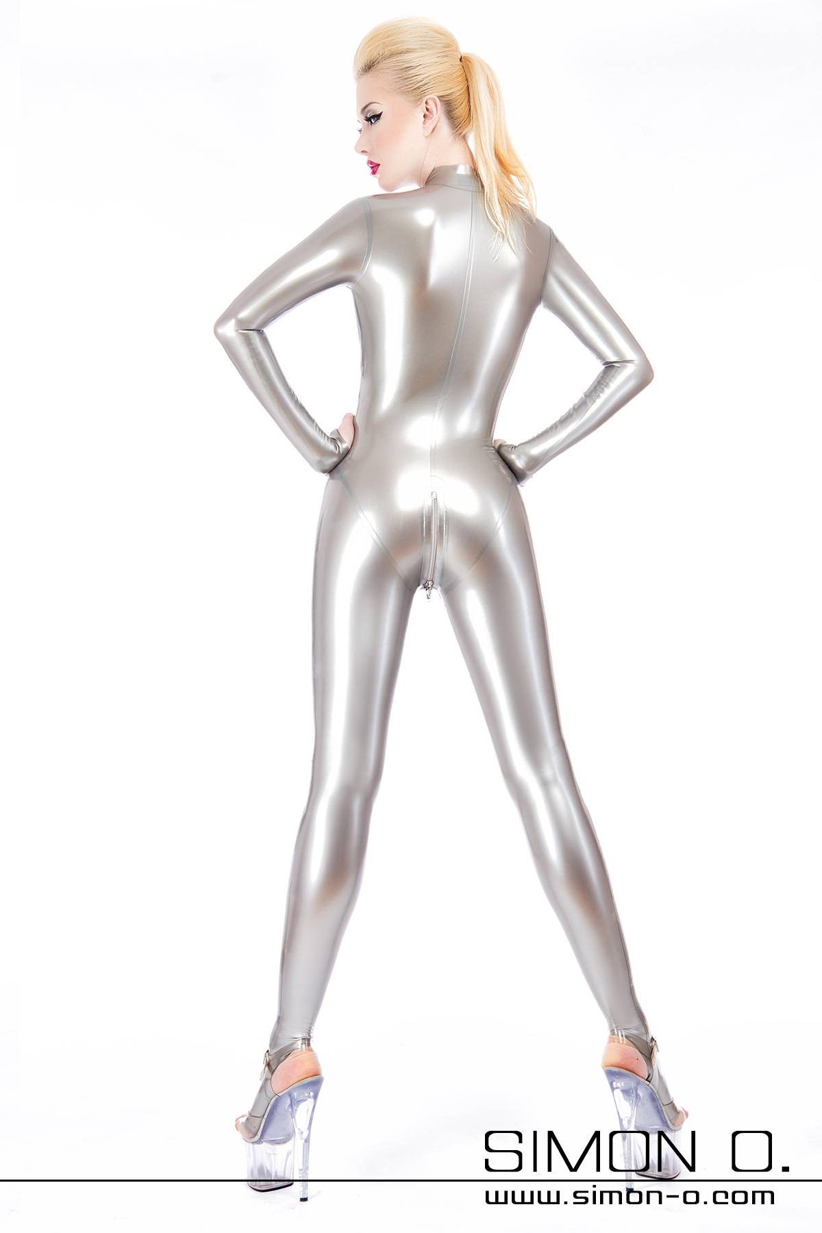 A blonde woman from behind in a skintight silver latex catsuit with zipper in the crotch area