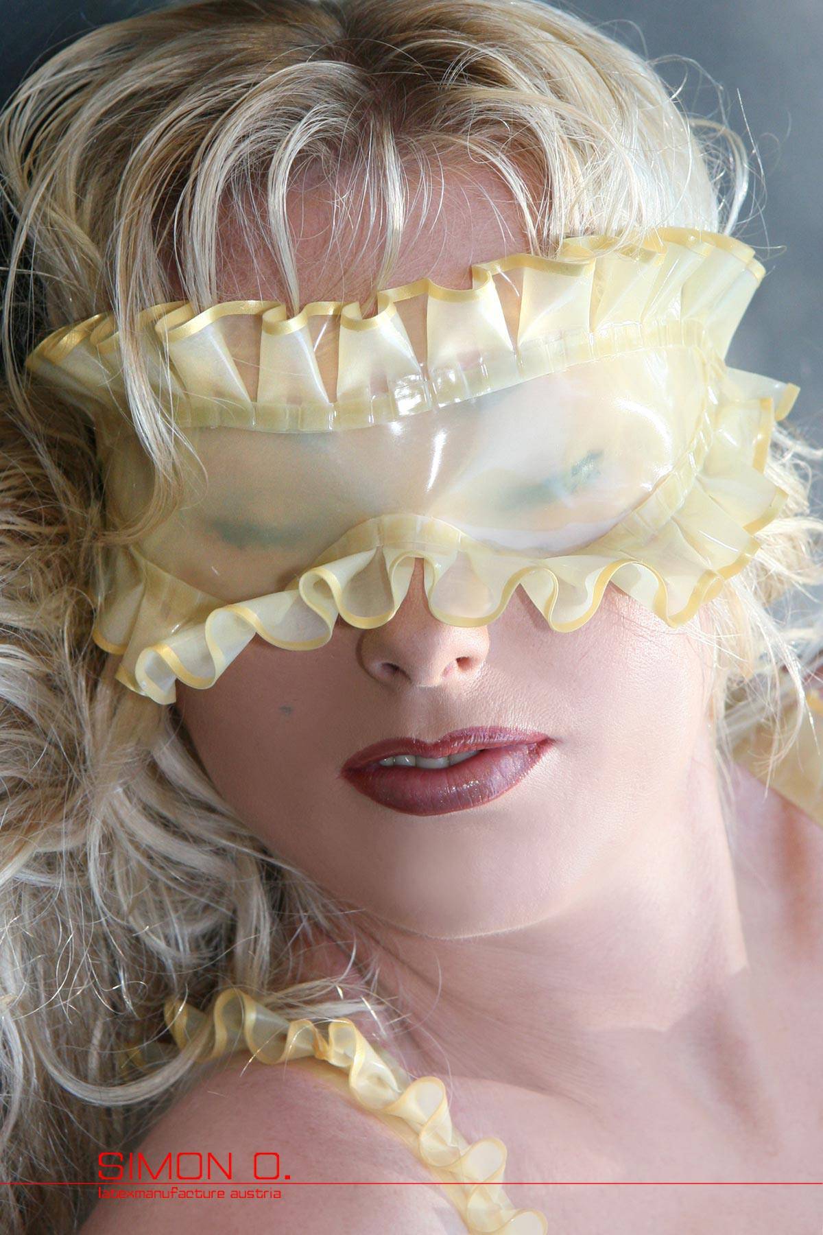 Eine blonde Damen mit roten Lippen trägt eine Latex Augenbinde