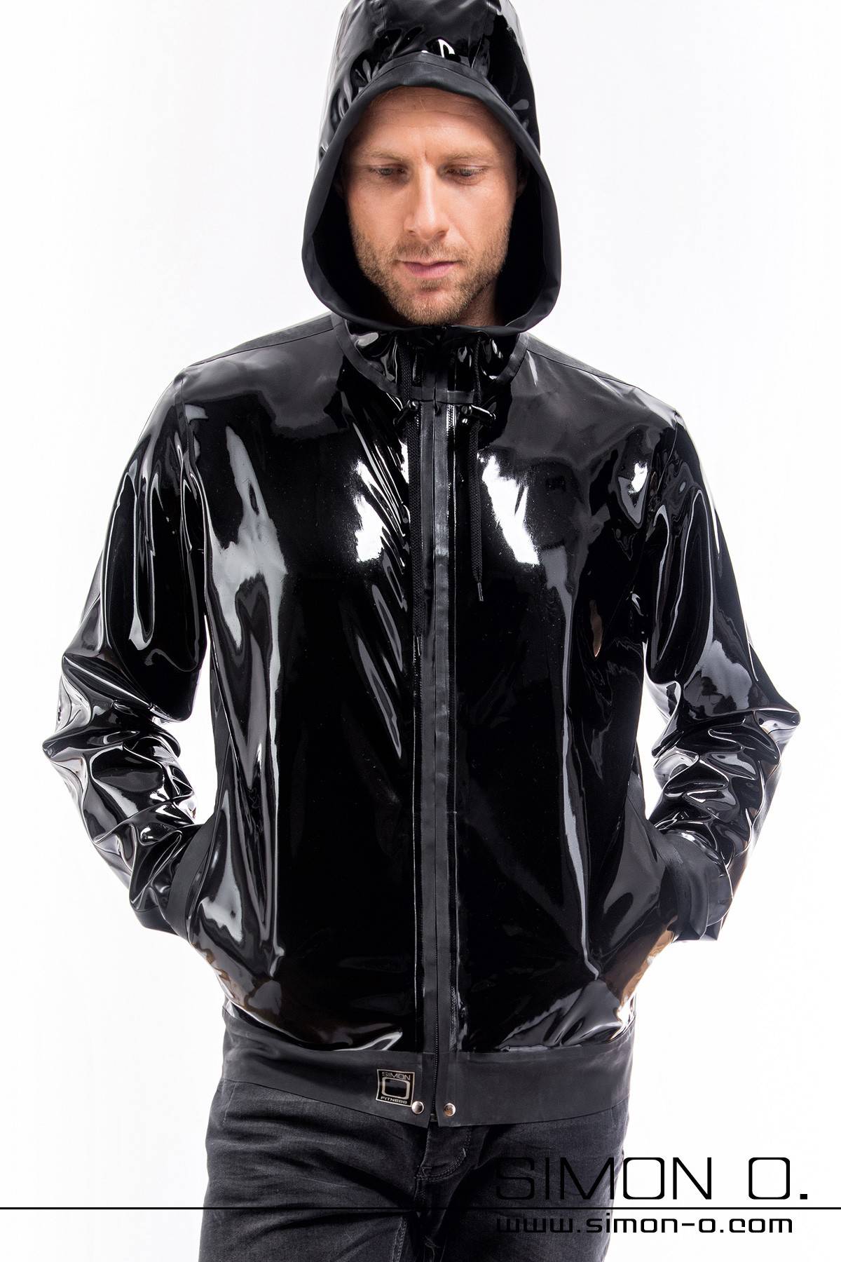 Ein Mann trägt eine Glanz Trainingsjacke aus Latex mit Kapuze in Schwarz