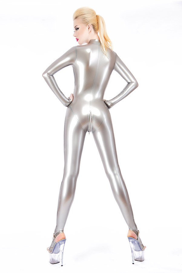 A person in a metallic silver latex bodysuit and high heels stands with her back to the camera. Her hands rest on her hips and her hair is styled into a high ponytail.