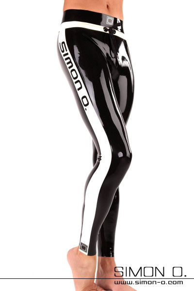 Close-up of a man wearing shiny black and white sporty latex leggings with ‘SIMON O.’ printed on the side. The person is standing barefoot in front of a plain white background.