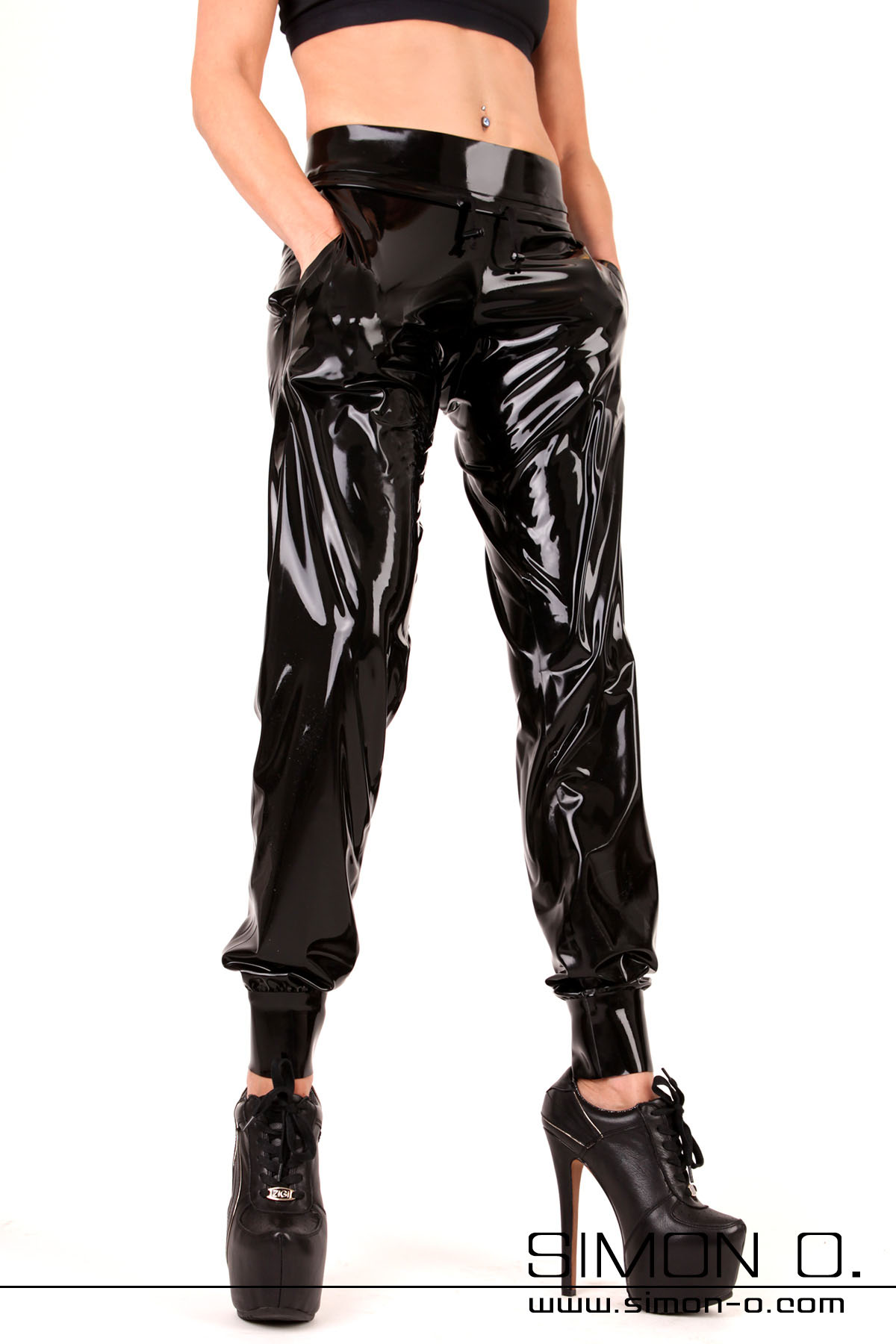 A woman in high heels wears shiny latex sweatpants with pockets.