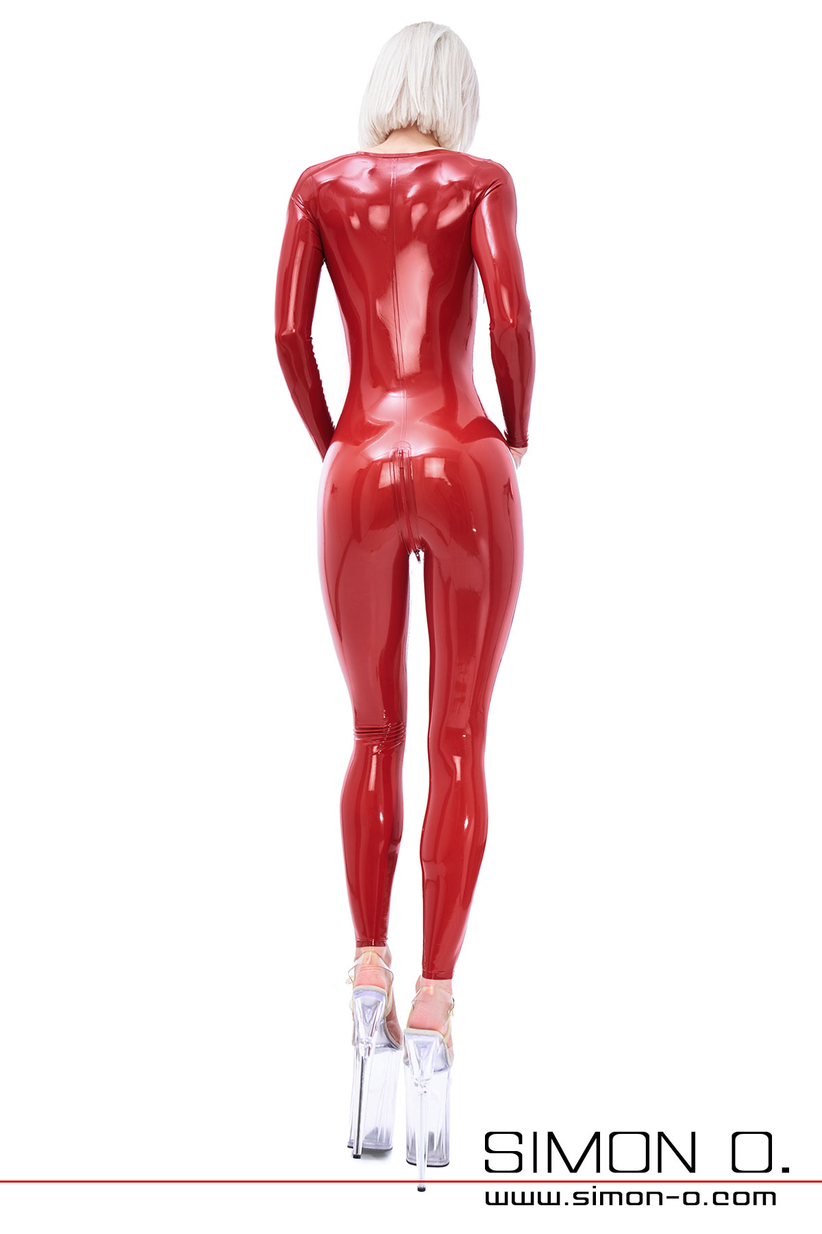 Eine Frau trägt einen hautengen langarm Latex Catsuit in Rot in Kombination mit High Heels. 