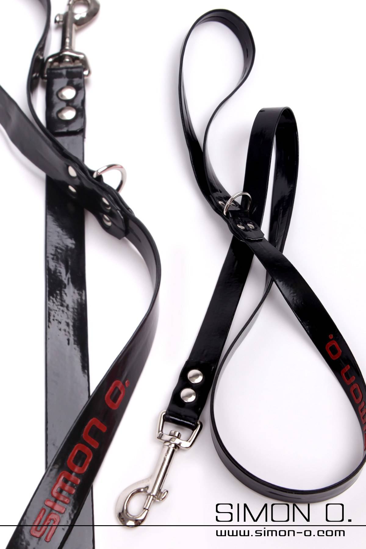 Two black latex leashes with metal fasteners are shown on a white background. SIMON O.’ is printed in red on one of the leashes.