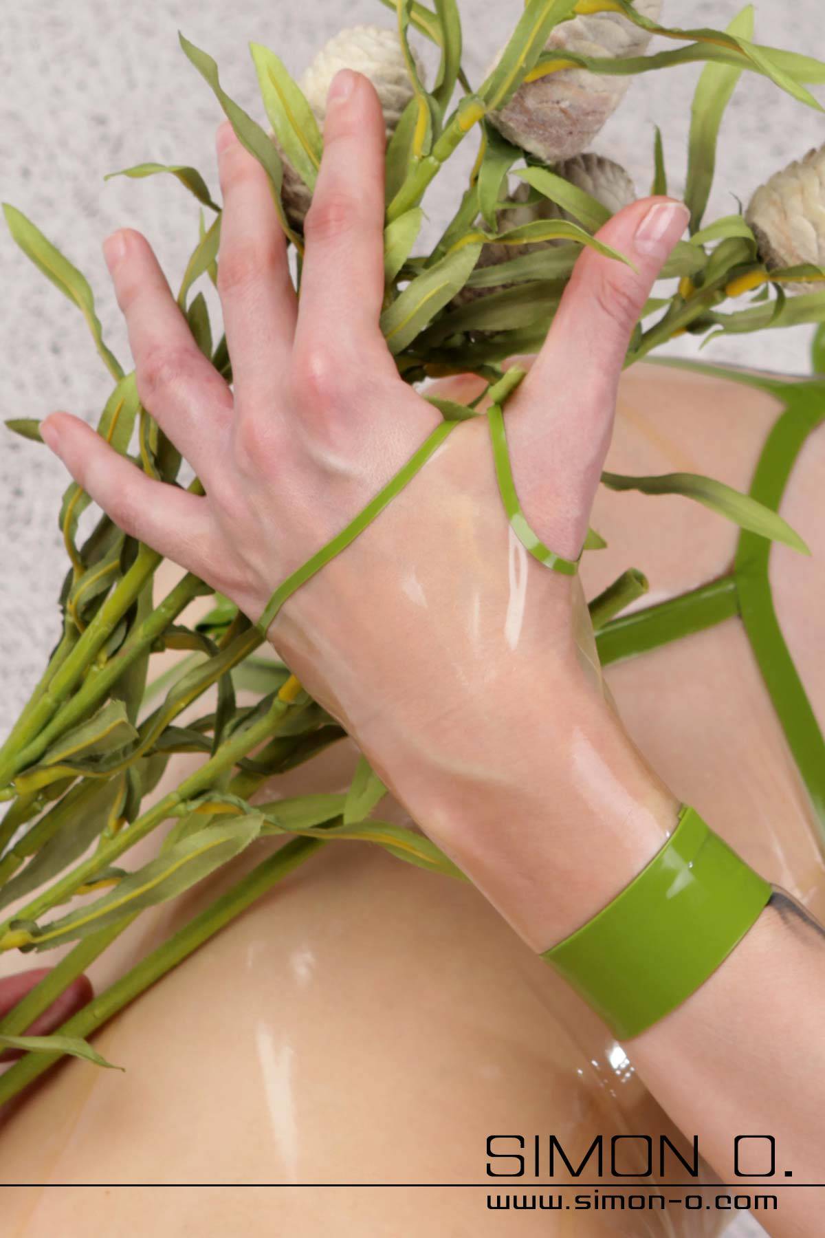 One hand with a transparent short gauntlet holds a bouquet of green leaves. The glove is transparent with green appliqués.